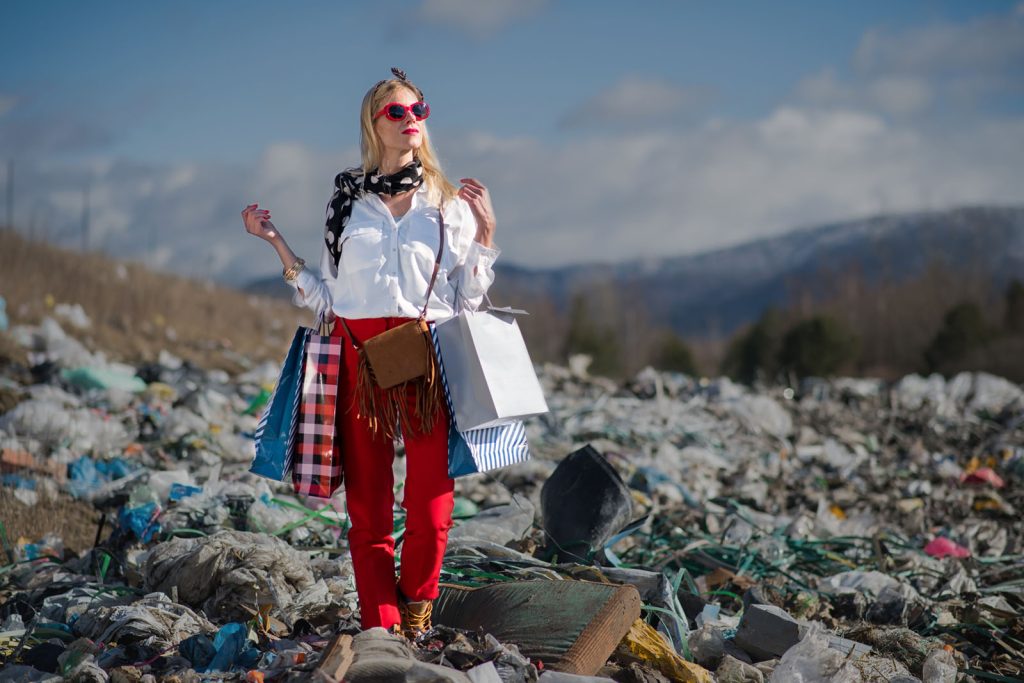 representation of fast fashion, blonde woman standing with shopping bags on top of waste // Healthier Me Today