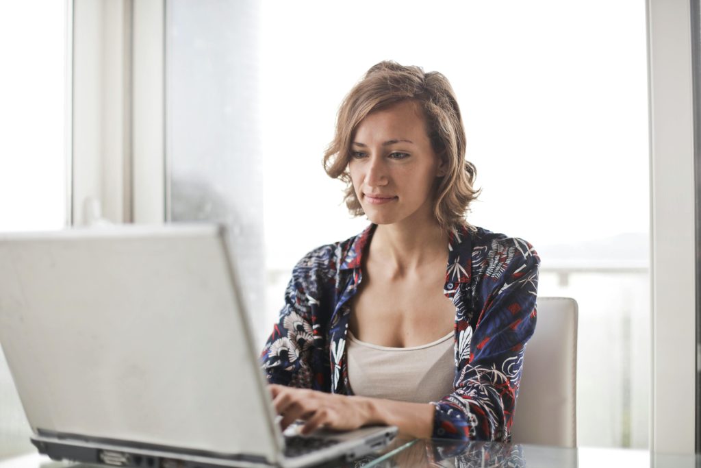 woman with blond hair, sitting at silver computer, window with light curtains // Healthier Me Today
