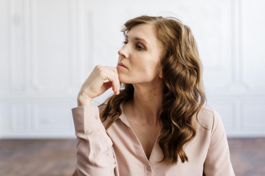 woman sitting, curly hair, white wall, looking to the side, sharp jawline, unhappy // Healthier Me Today