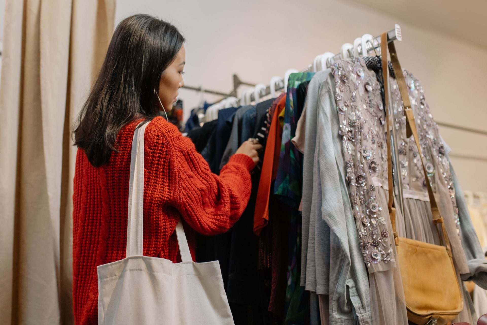 woman with black hair, thrifting, wearing a white toto bag and a red sweater, rack of different clothes // Healthier Me Today