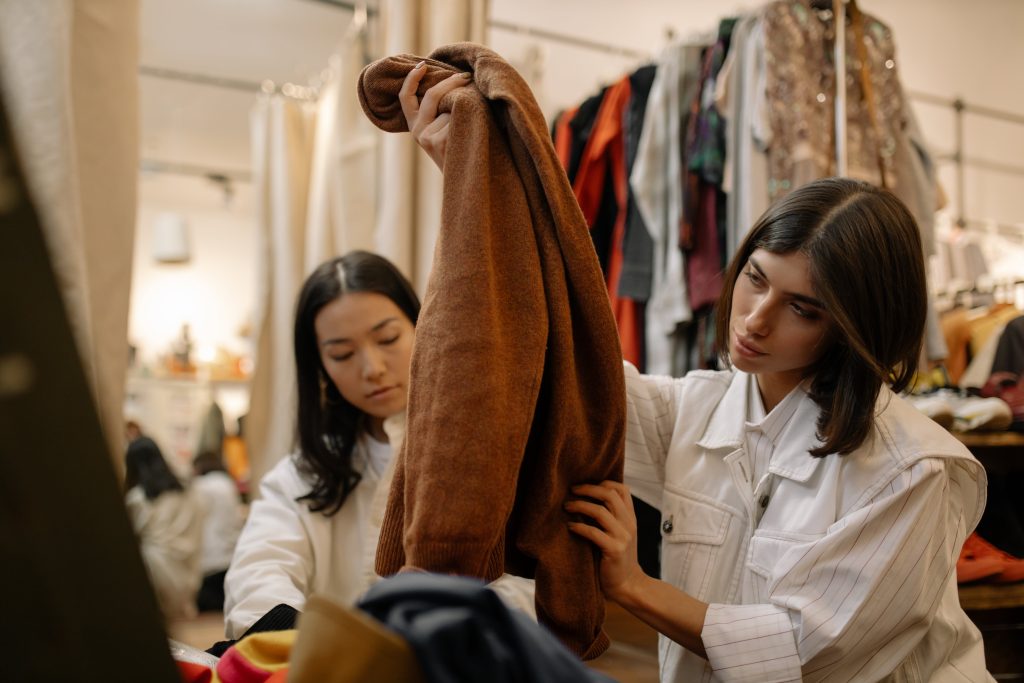 two dark hair woman, thrifting, woman holding brown sweater // Healthier Me Today