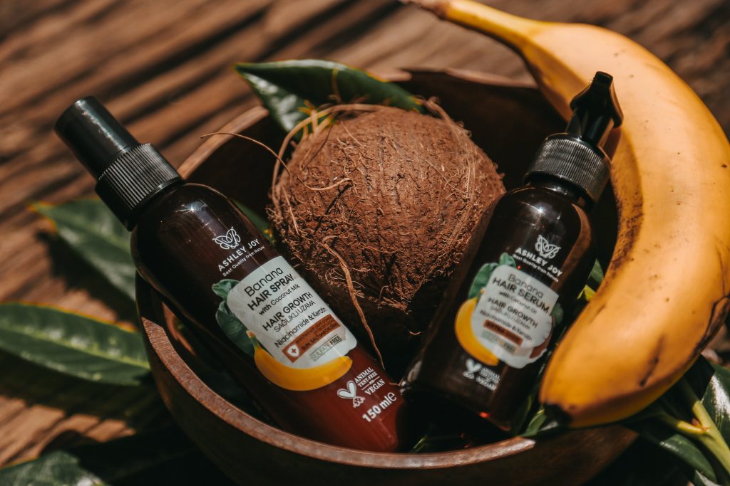 hair care products placed in wooden bowl, surrounded by banana and coconuts , on wooden table // Healthier Me Today