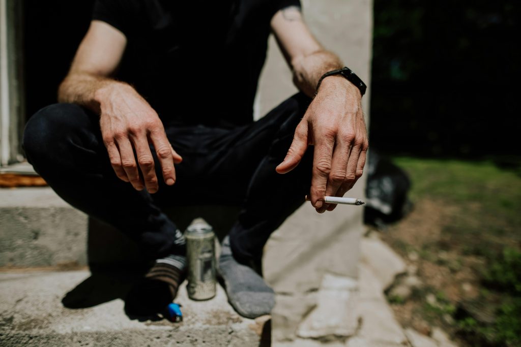 man sitting on step, wearing socks, cigarette in hand, grass not taken care of // Healthier Me Today 
