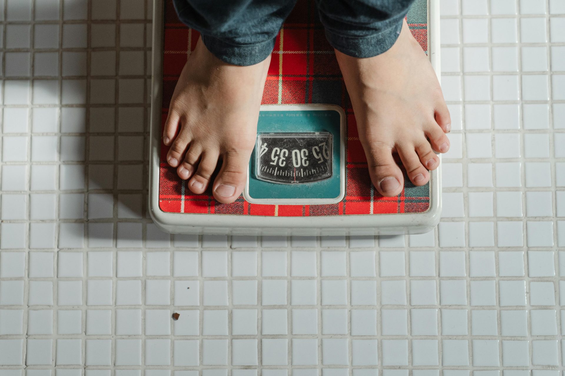 man stepping on scale, red and white scale, man wearing jeans, white titled floor // Healthier Me Today