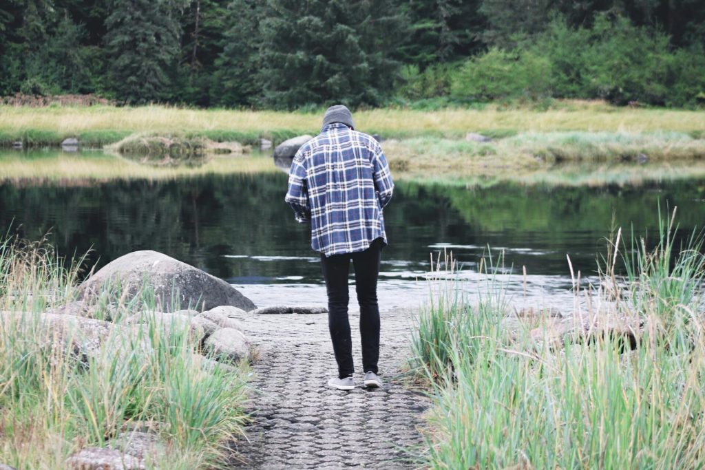 man walking alone, wearing checked shirt, river, grass, concrete pathway, green bushes // Healthier Me Today