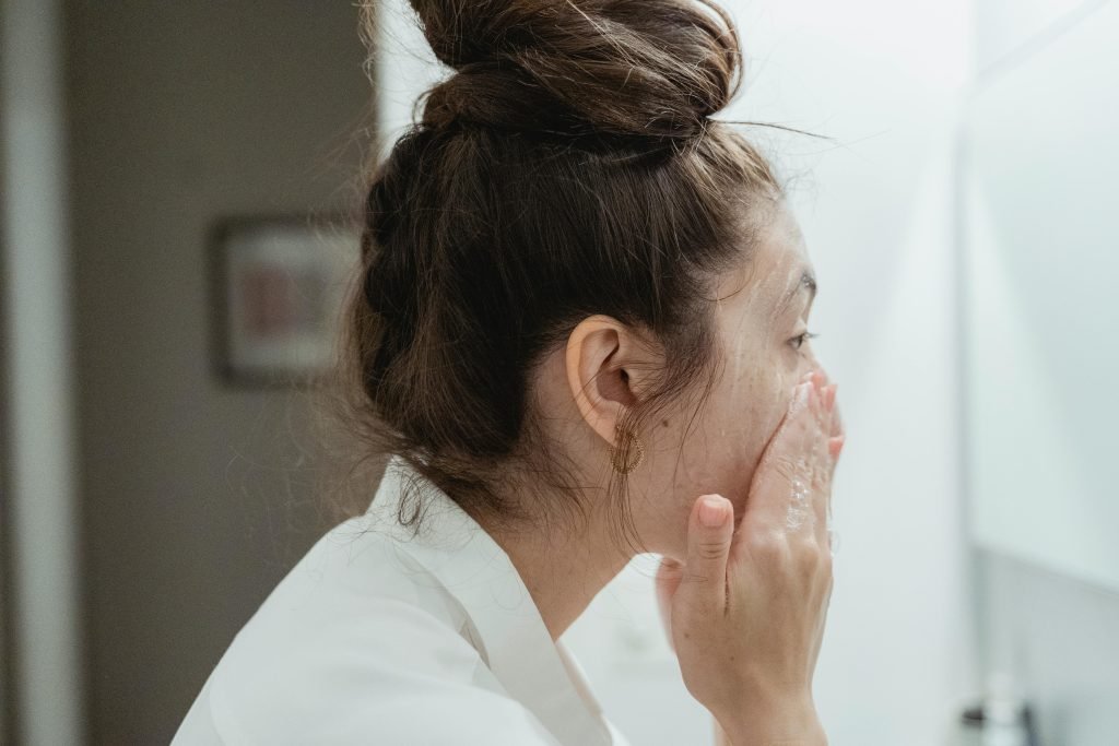woman in white robe, washing her face, dark hair, hair in a bun, looking into a mirror, blurred background // Healthier Me Today // Best Face Wash, benzoyl peroxide face wash
