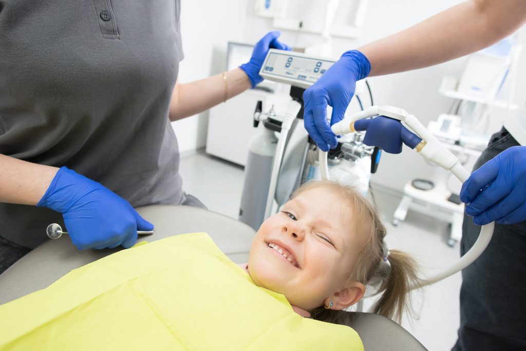 kids dentist, young kid with blond hair, laying on dentist chair, smiling