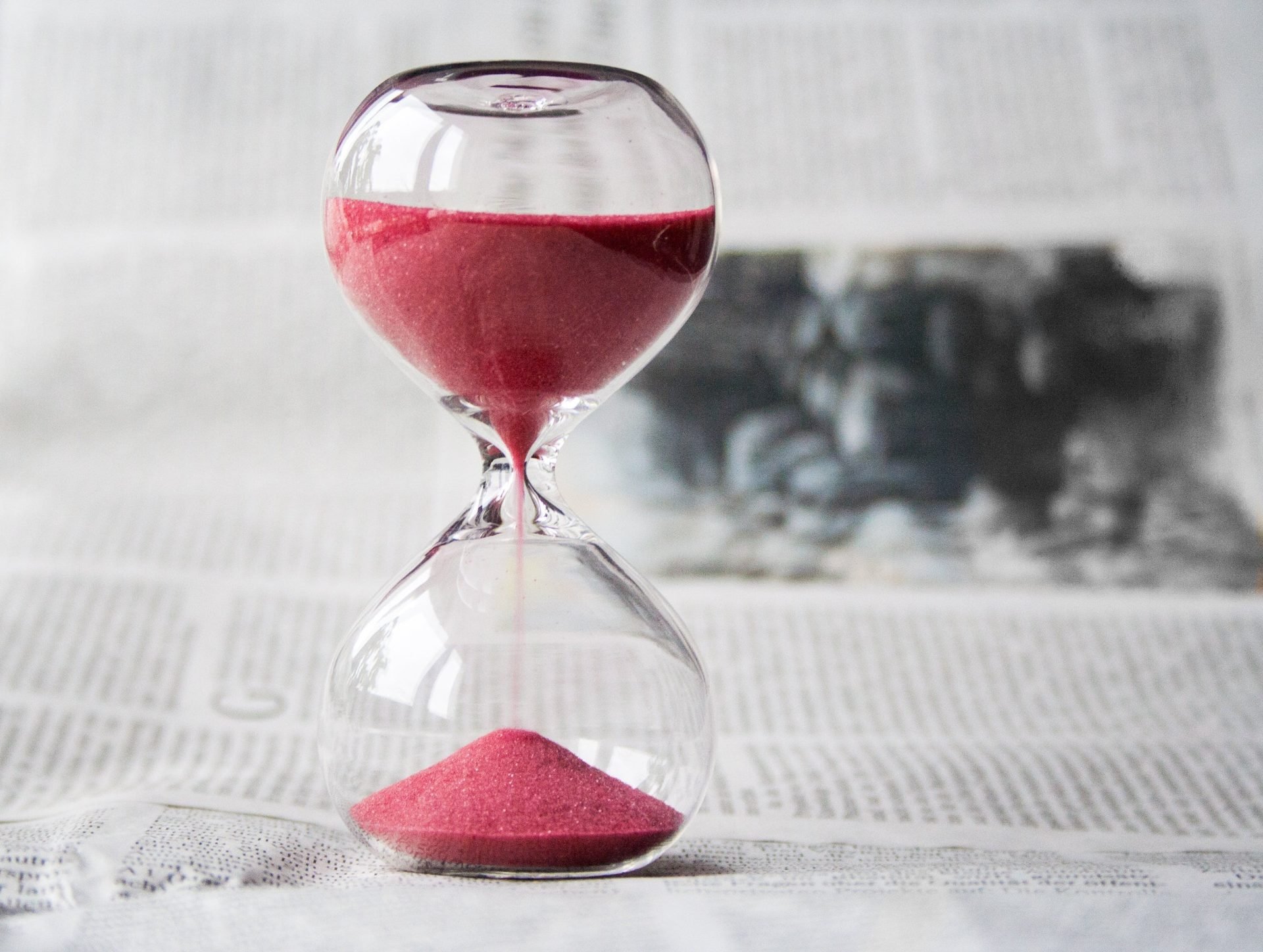 hour glass, time running out, red sand in glass, newspaper in background // Healthier Me Today
