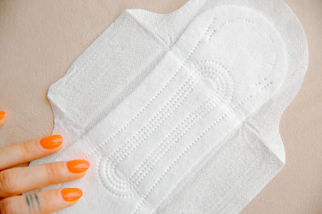 period pad with wings, woman touching it with hand, orange long nails, pink counter // Healthier Me Today 