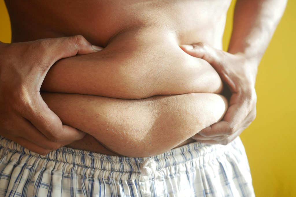 man, holding stomach fat, shirtless, in boxers, yellow wall // Healthier Me Today