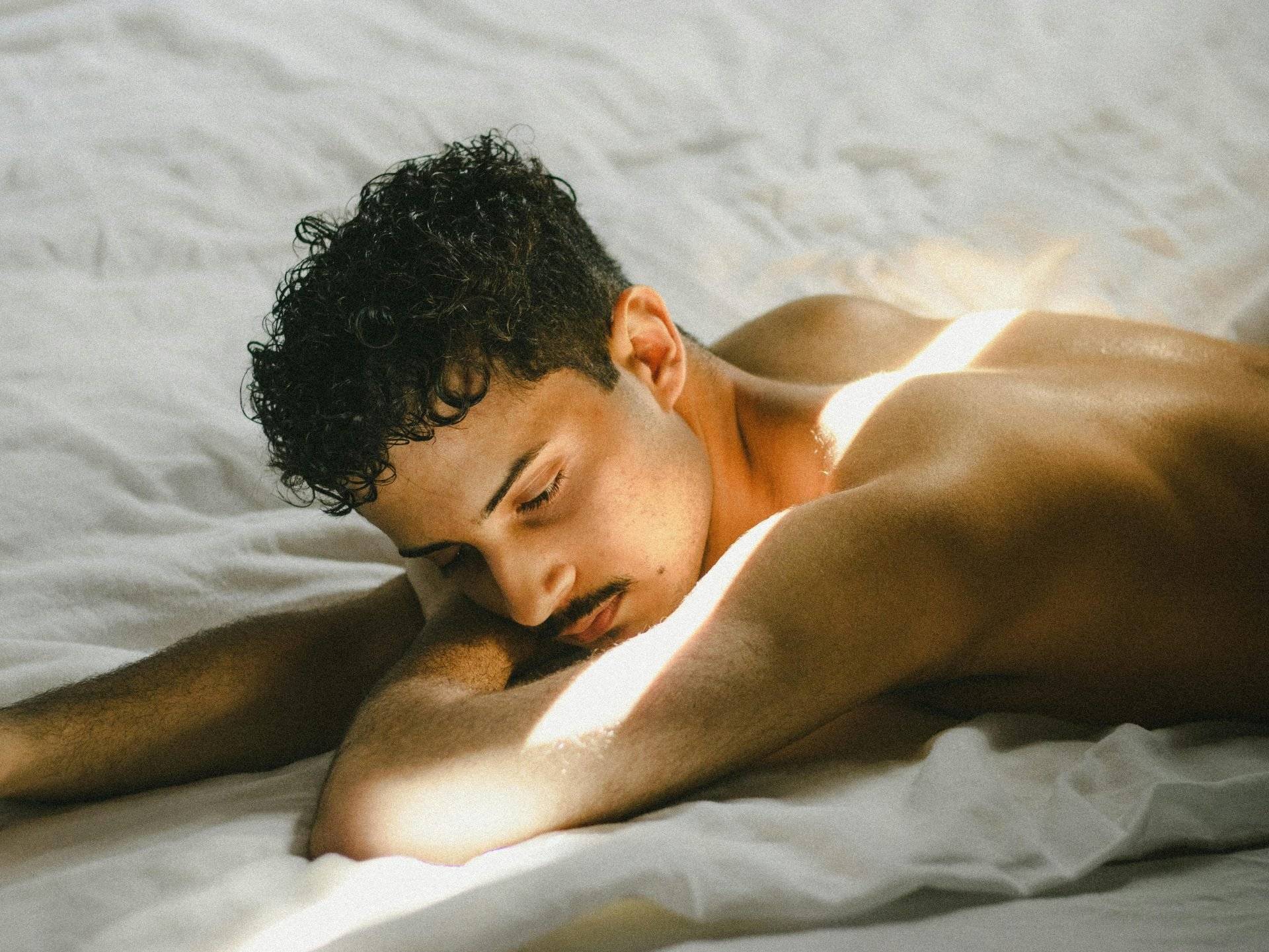 body positive: man laying shirtless, sun shining on man, white sheets // Healthier Me Today